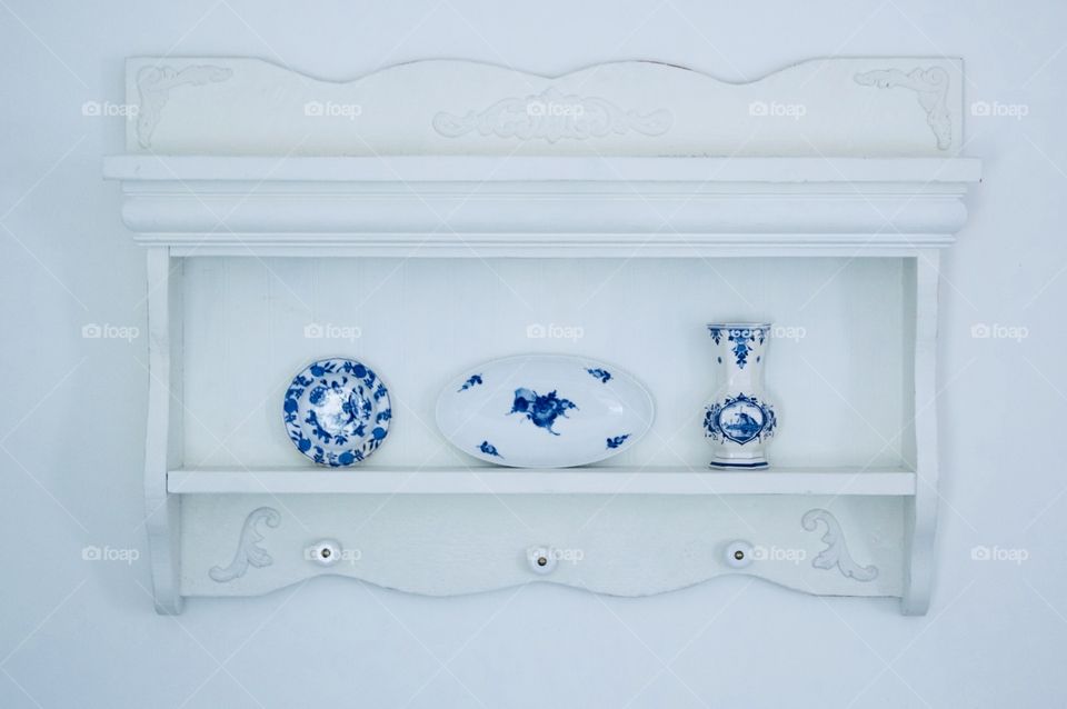 Delft Blue porcelain round dish, oval dish, and vase on a white vintage shelf against a white wall