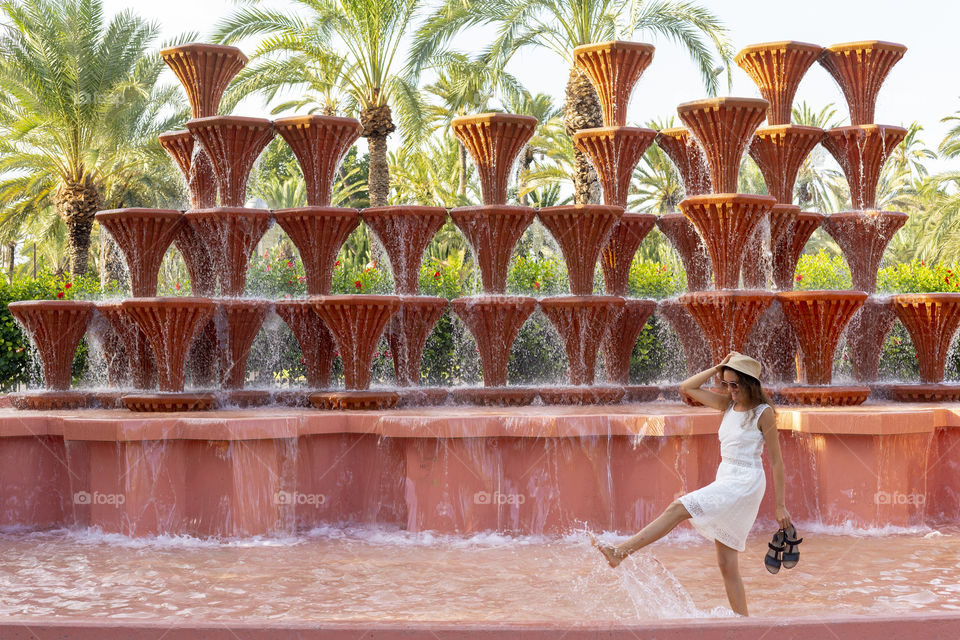 Happy millennial girl is having fun in the fountain (Spain, Elche)