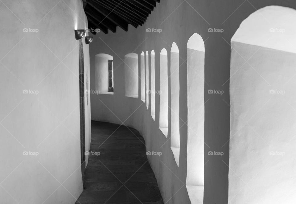 A beautiful view of the ancient passage in the castle with white walls, a wooden floor and windows in the form of arches, close-up on the side. The concept of medieval architecture and castles.