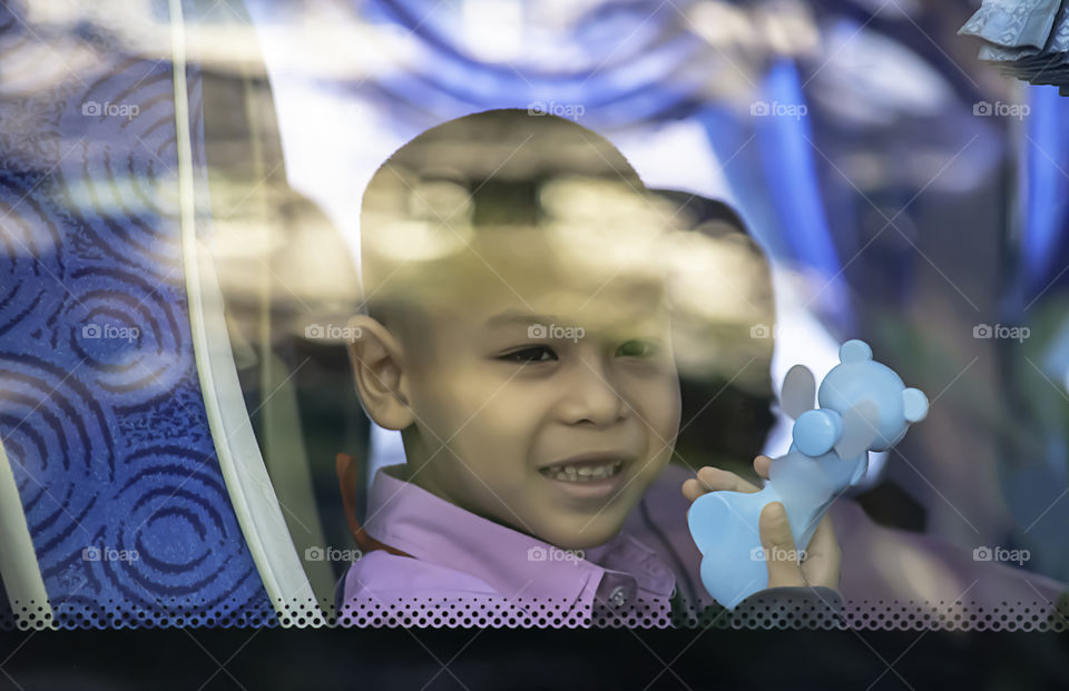 Asian boy holding the portable small fan sitting on a school bus.