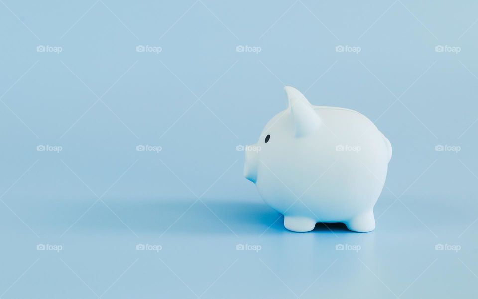One light blue piggy bank stands sideways on the right on a light blue background with copy space on the left, close-up side view. Business and finance concept, blue on blue.