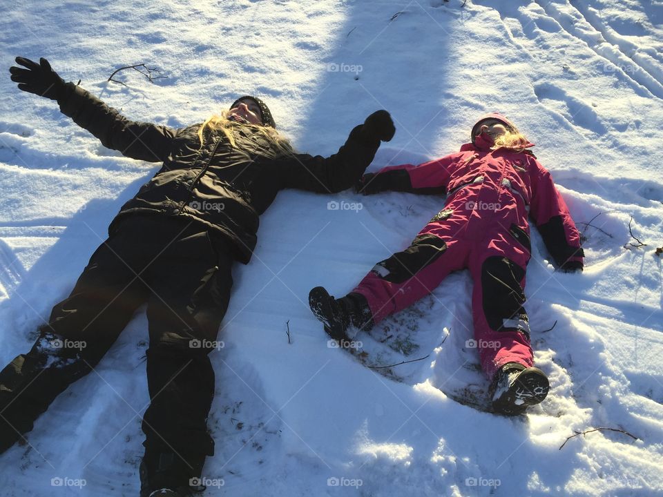 Mom and doughter playing in the snow making snow angels.