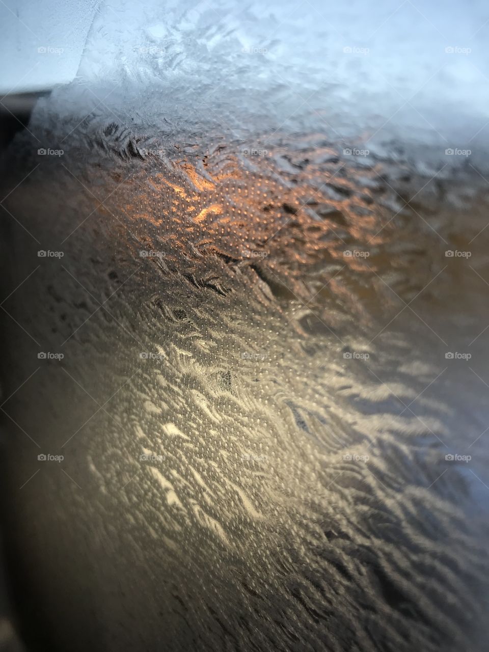 Beautiful ice pattern on a window with the sunrise behind. Waves pattern off ice.