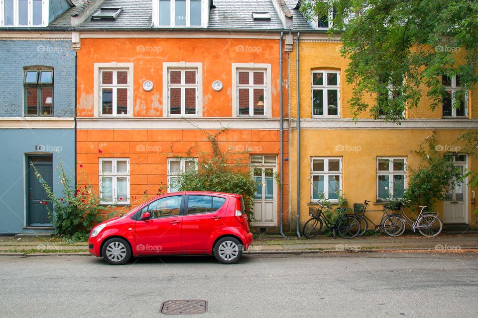 Red car parked in the street in front of three colorful old houses