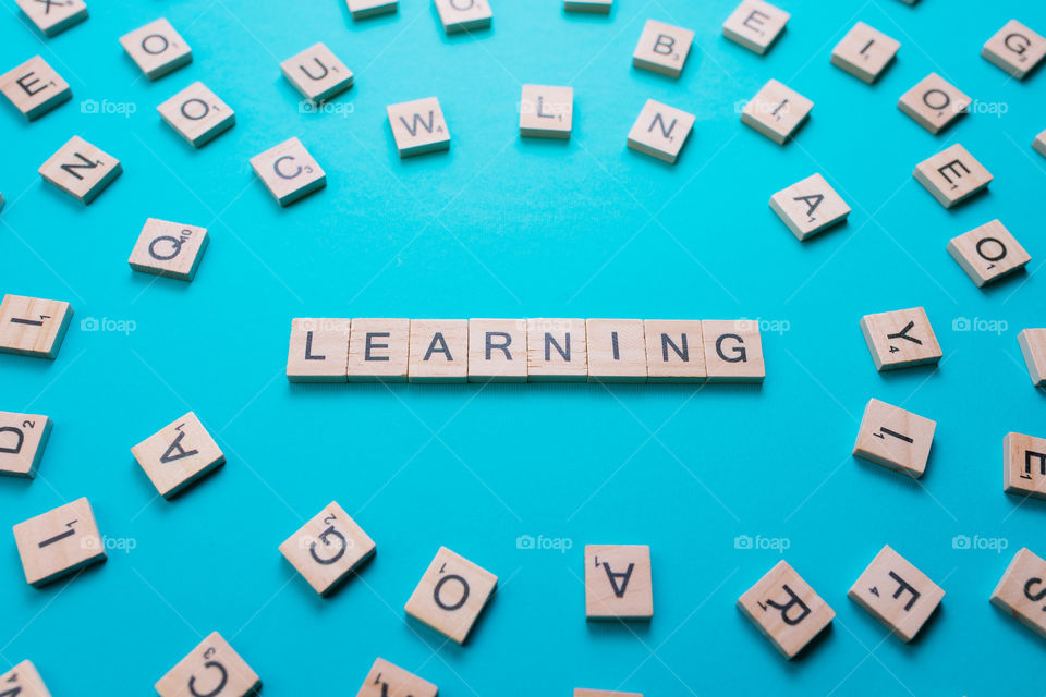 Word Learning formed by wooden letters in the composition center with all the letters of the alphabet on a light blue background