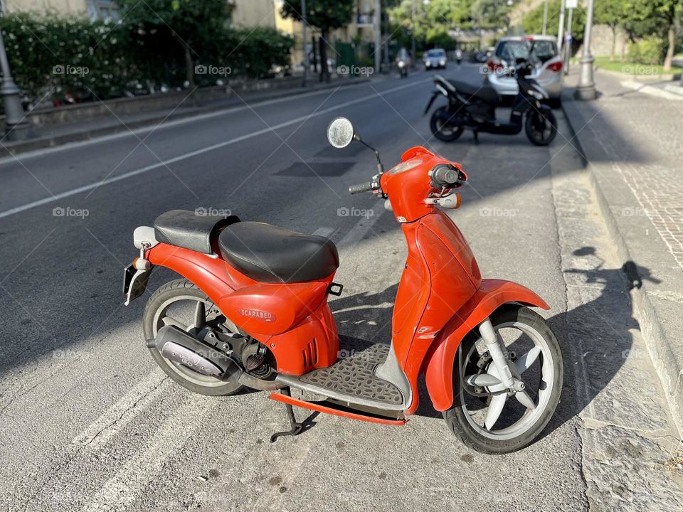 Red scooter parked on the side of the road 