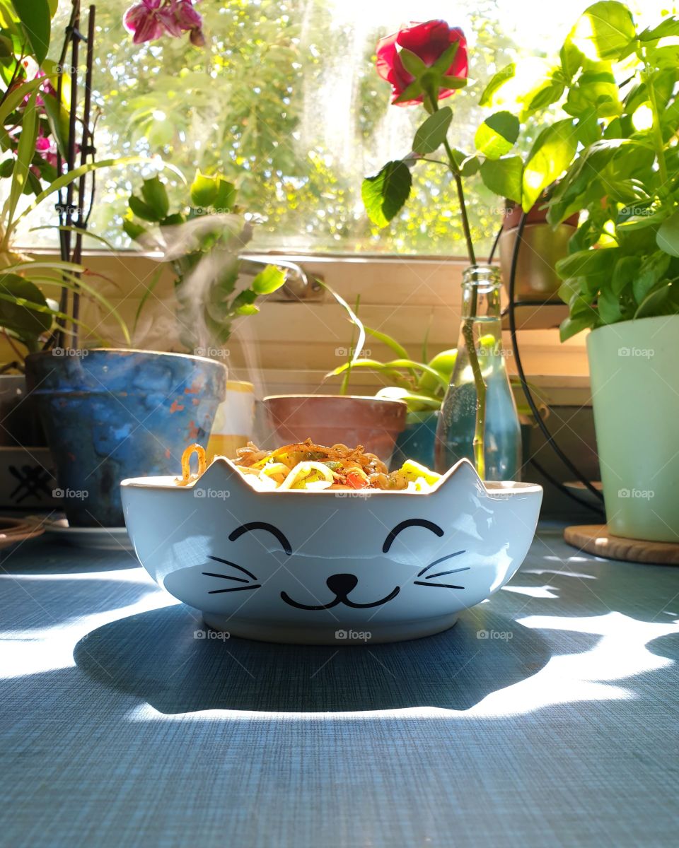 A bowl with cat ears and a cat face, filled with steaming fried noodles.