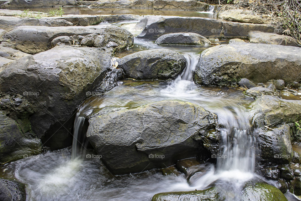 The water flowing over rocks and trees down a waterfall at Khao Ito waterfall , Prachin Buri in Thailand.