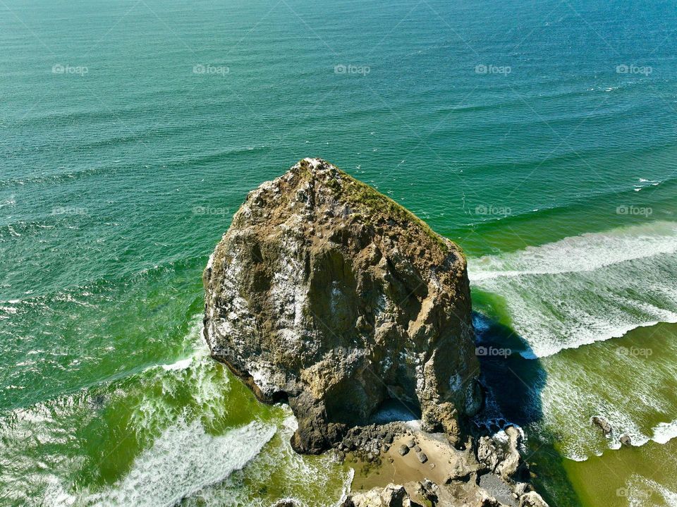 An awe-inspiring bird’s-eye view of Haystack Rock, standing tall against the endless expanse of the Pacific Ocean. This iconic monolith, rising 235 feet above the shore, is a testament to the rugged beauty of Cannon Beach, Oregon.