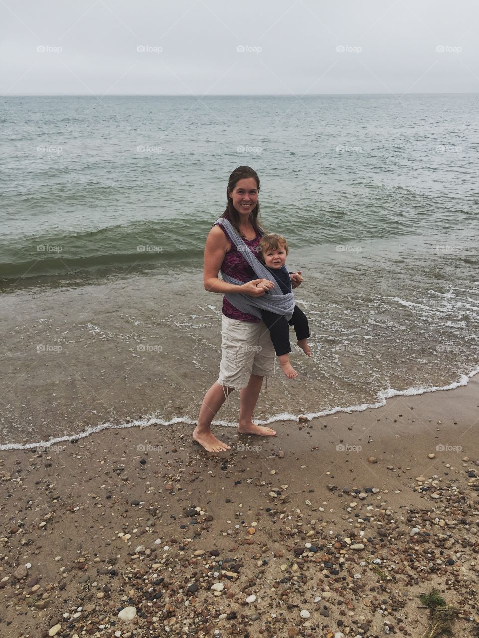 Happy woman carrying her son and standing at beach