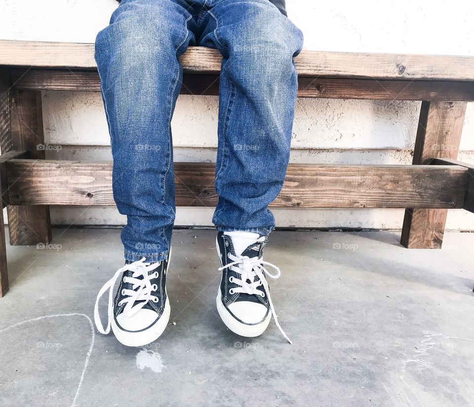 Boy sitting on the bench wearing blue jeans and converse styles shoes 