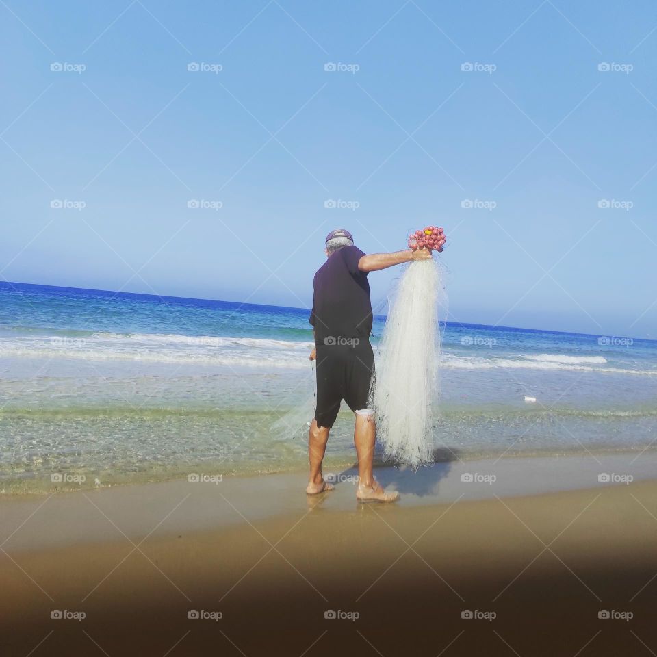 Image of a fisherman preparing a fishing net on the seashore