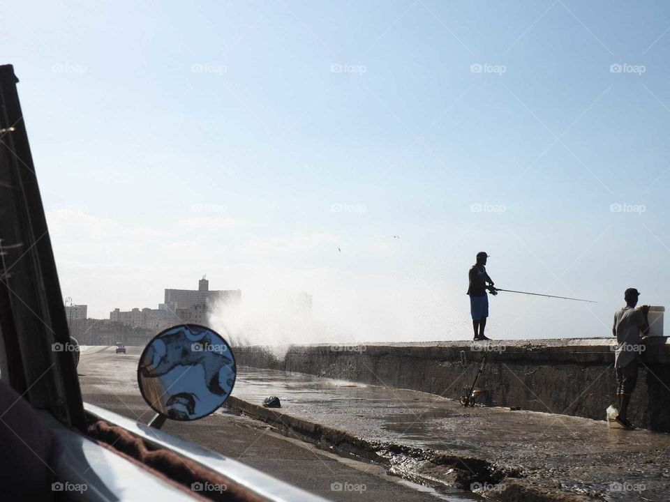 Fisherman on the Malecón in Havana, Cuba during sunset with romantic lightning and dramatic waves.