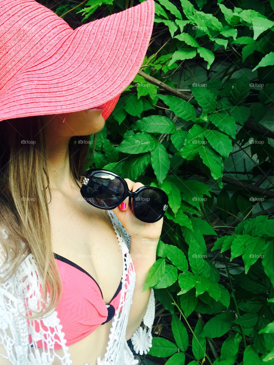 Selfie of woman with long dark blonde hair with black sunglasses in her hand standing against background made of leaves