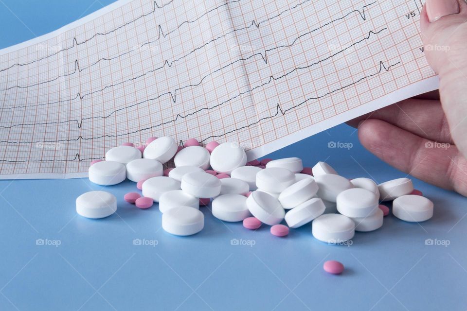 Pills and medicines lie on a blue background with an electrocardiogram of the heart.