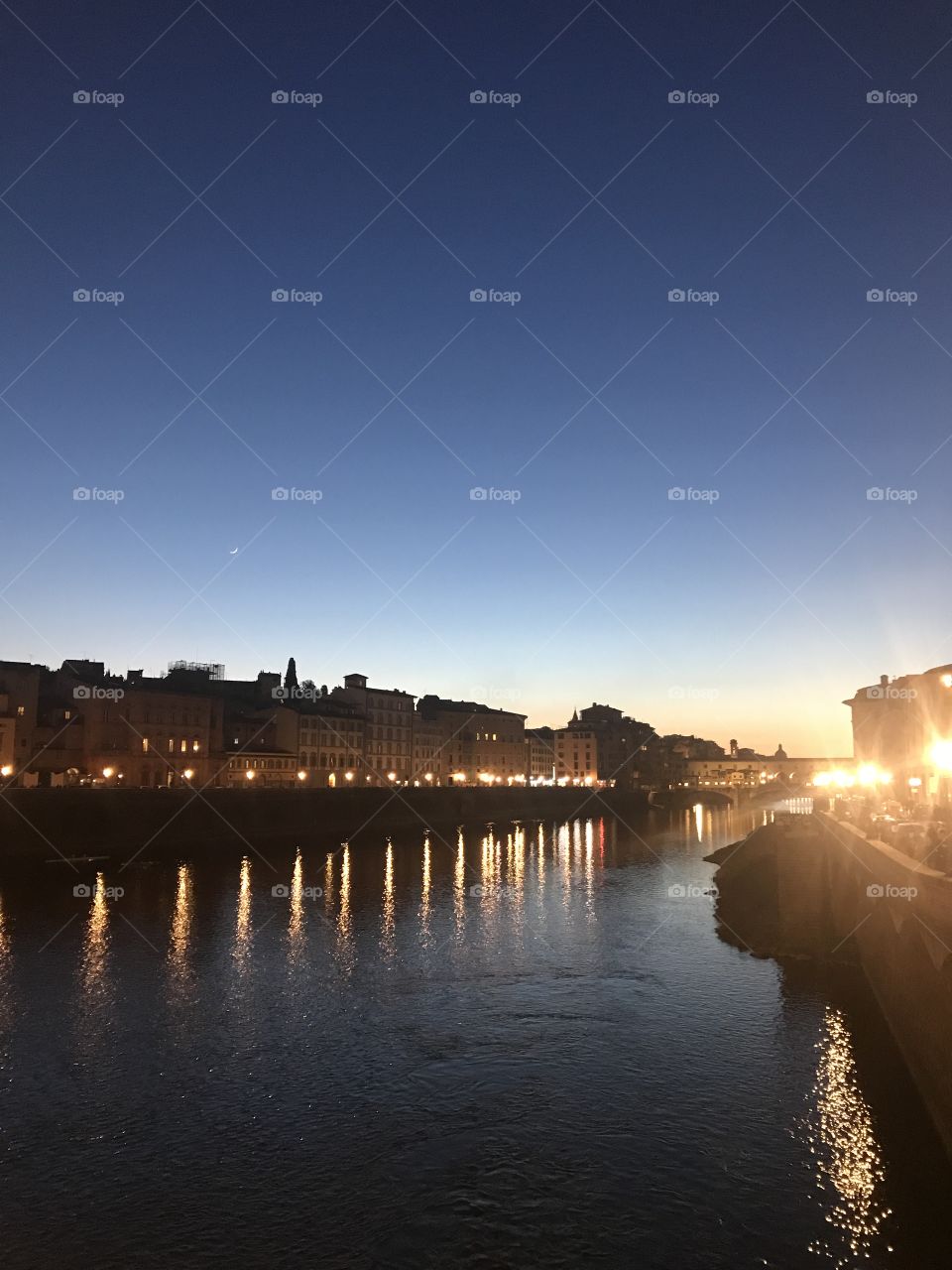 The Arno river and the Ponte vecchio lit by the moonlight and street lights surrounded by the gradient evening sky.