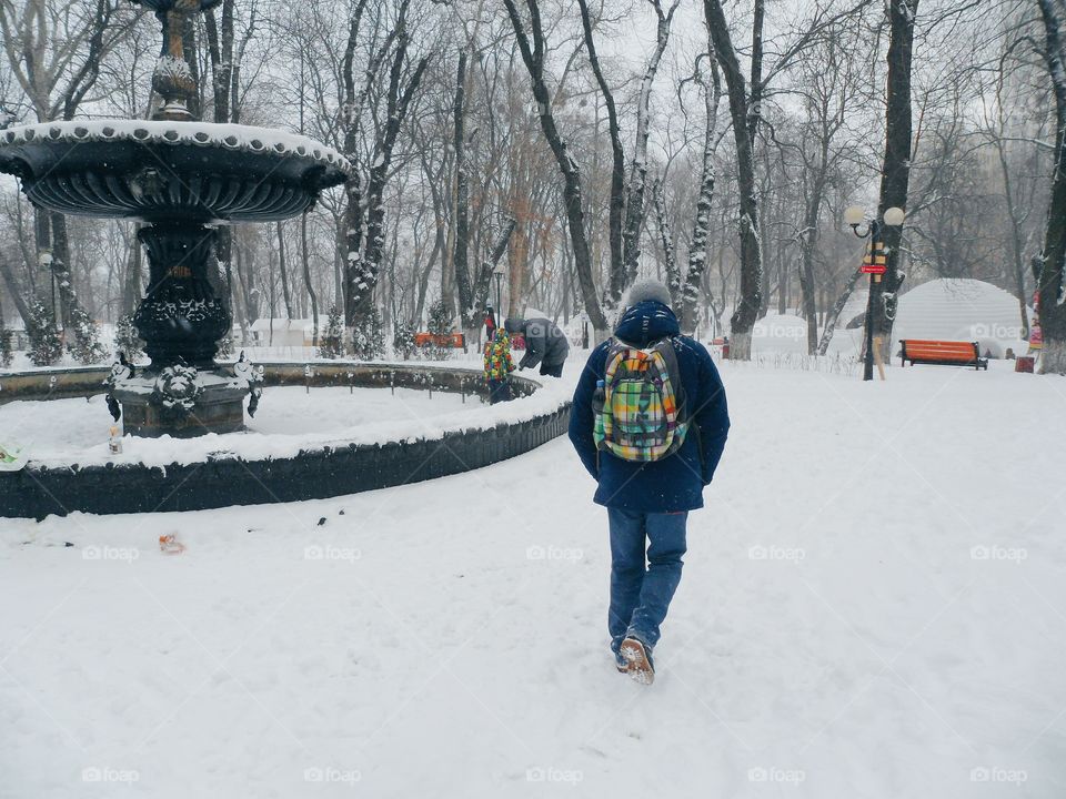 a man with a backpack walking in the winter park in the city of Kiev