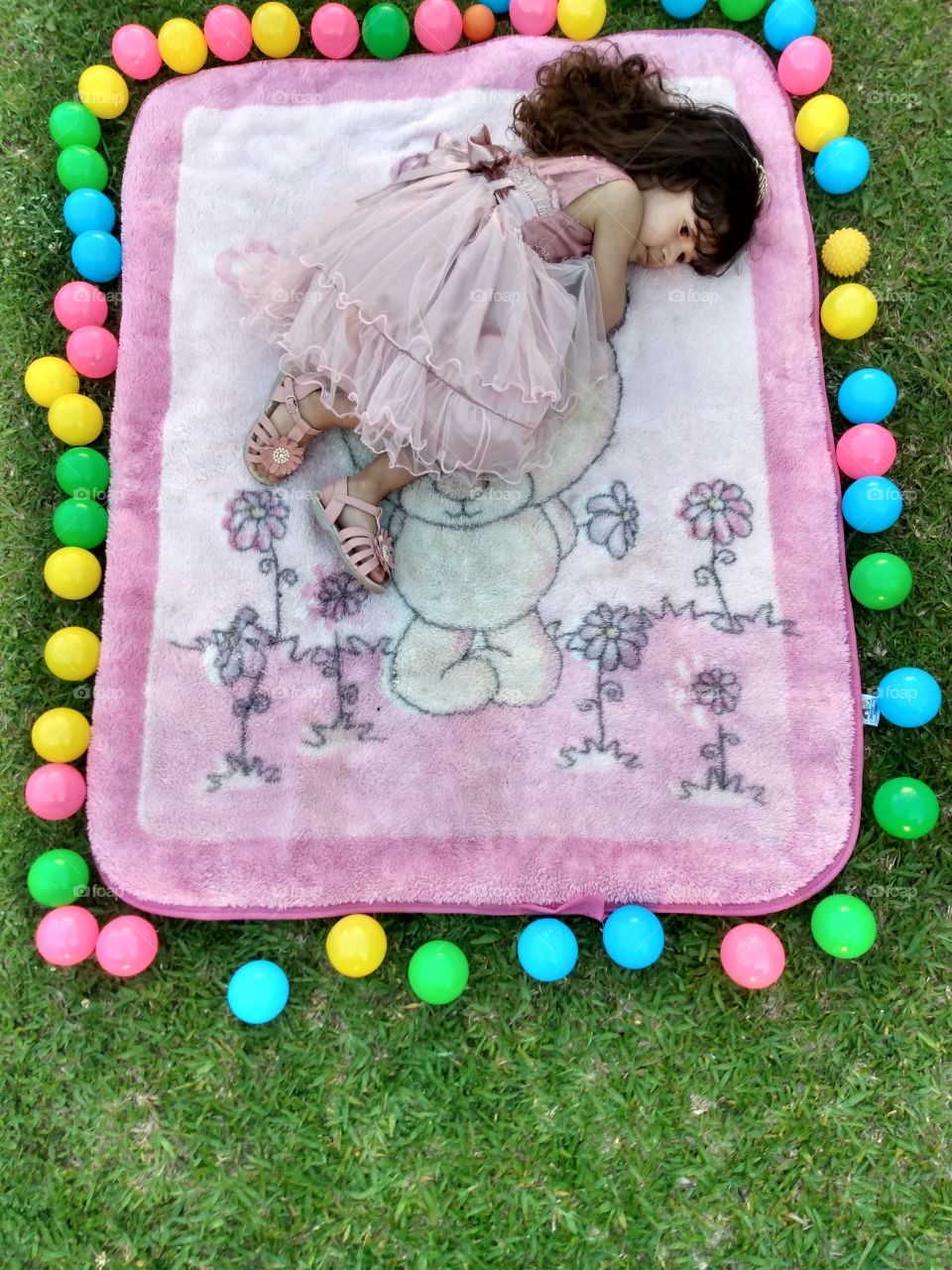 menina de 3 anos deitada no cobertor e a sua  volta tem várias bolinhas coloridas.