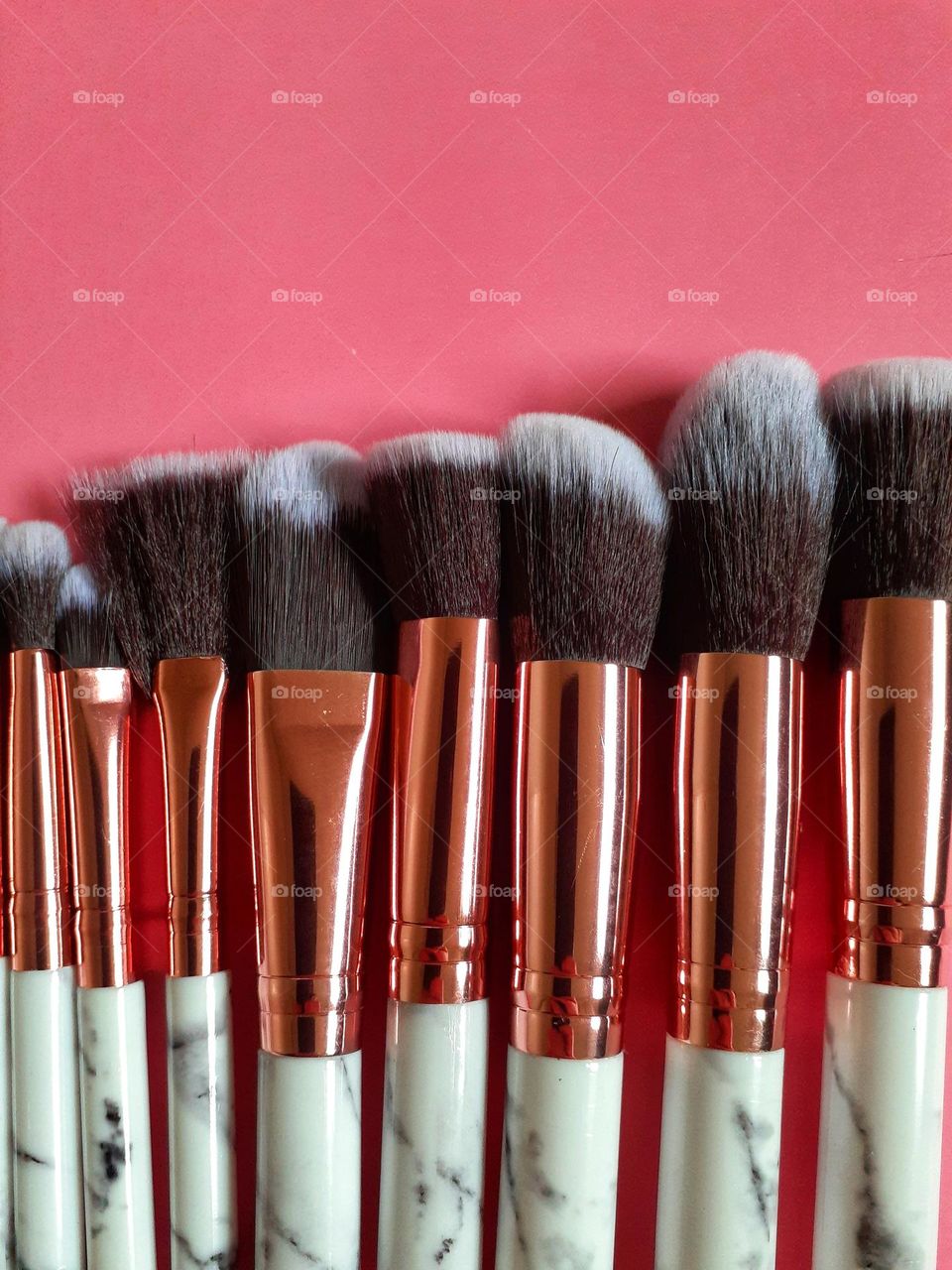 Makeup brushes in varying sizes, some thinner and some thicker are mined up on pink paper.