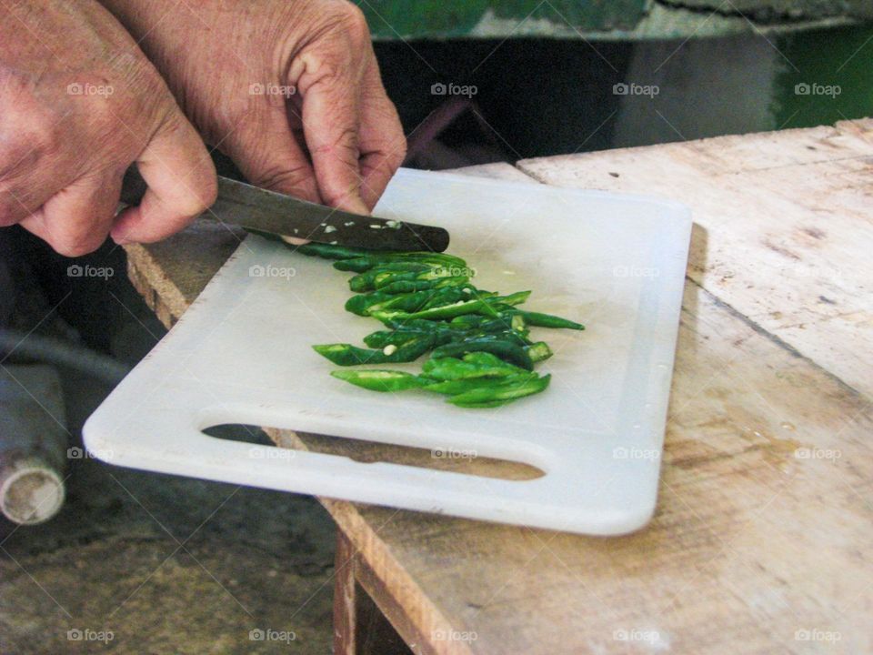 Portrait of a person cutting green chilies on a white cutting board