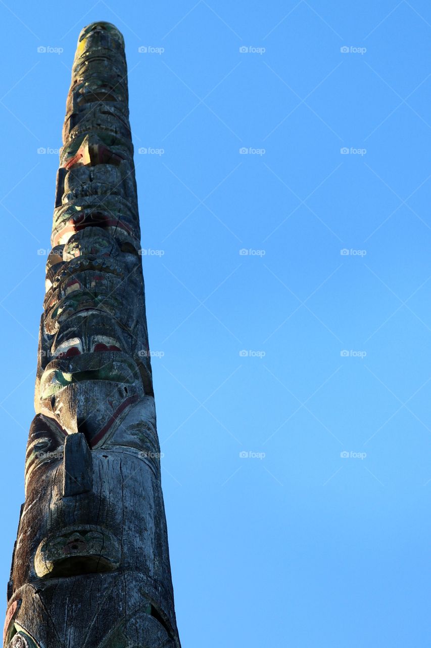 West coast Coast Salish First Nations Aboriginal carved wood totem pole against clear blue sky, Vancouver British Columbia Canada, minimalism 