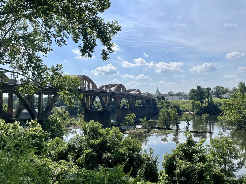 Trees, a lake, greenery, and a beautiful bridge on a sunny day . The reflections can be seen in the water