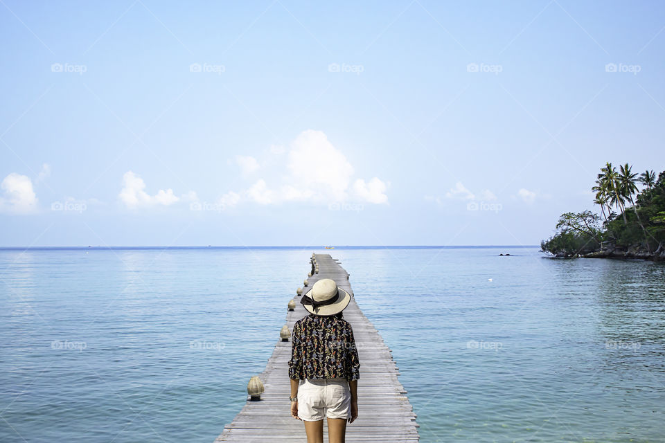 Asian Women  Wear a hat on wooden bridge pier boat in the sea and the bright sky at Koh Kood, Trat in Thailand.