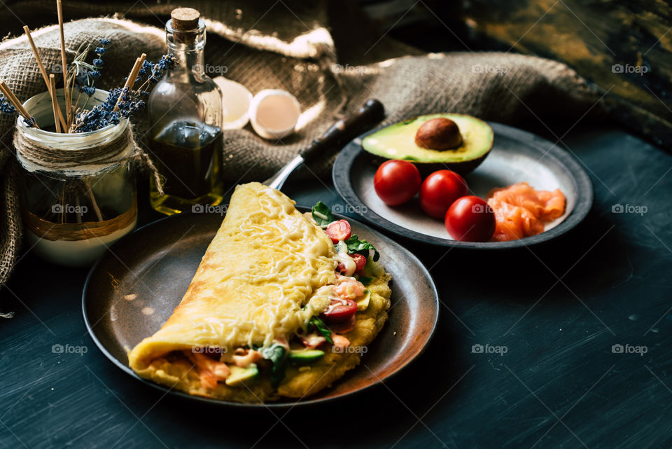 fresh, fluffy omelette with salmon, tomatoes, avocado, cheese and rucola, on a wooden rustic table