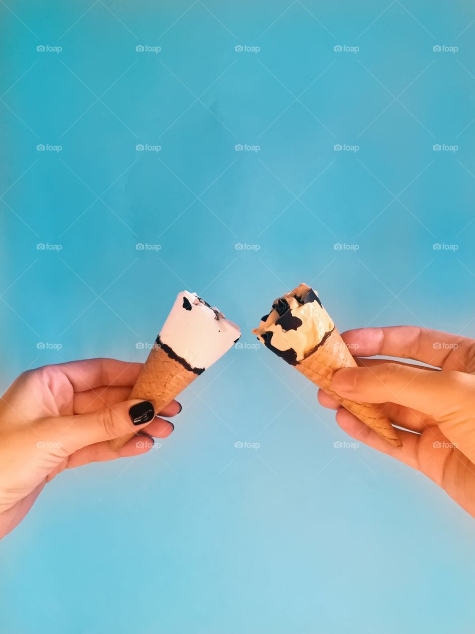 Two people holding ice cream against blue background