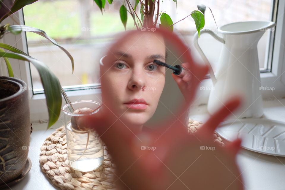 Young woman mirror reflection doing make up routine 