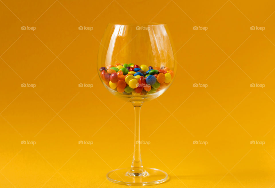 Sweet colorful candies in a glass on yellow background, minimalism