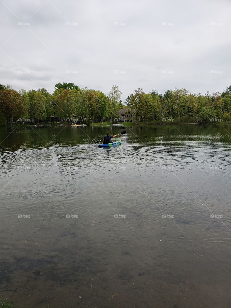 Solo kayaker enjoying the calm lake, midday. Muskoka, Ontario.