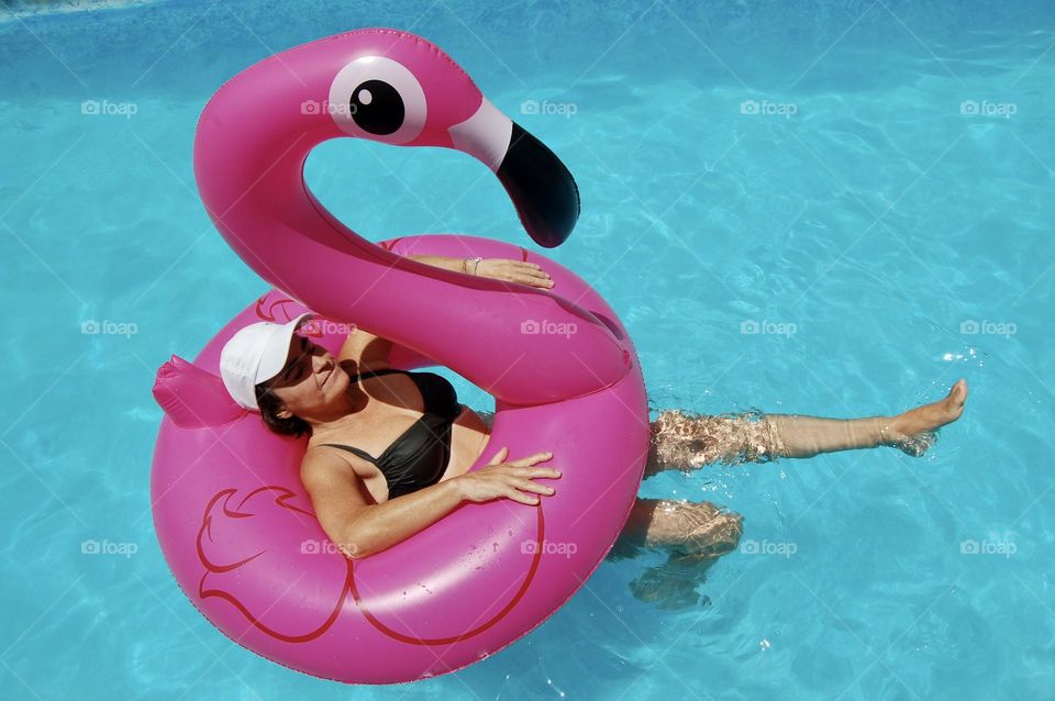 Woman floating with pink flamingo in swimming pool 