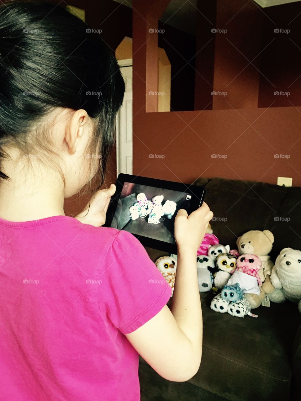 Little girl using technology of tablet to record a video of her stuffed animals 