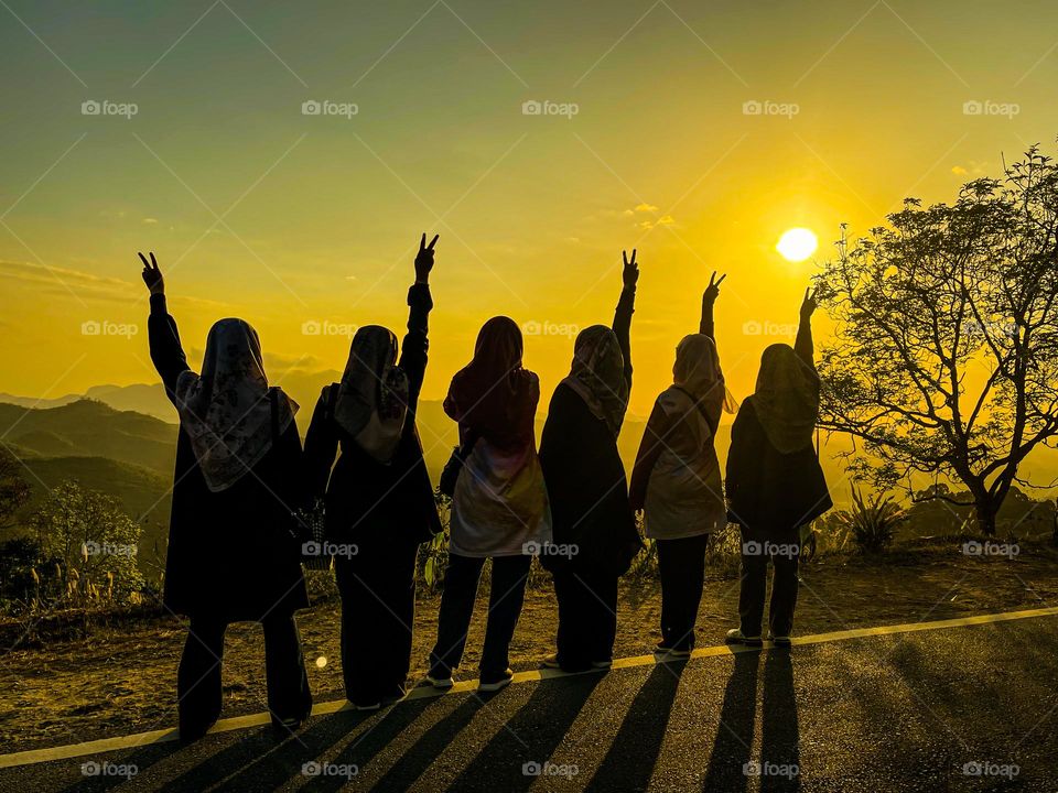 A group of happy girls on vacation looking at the sunrise and showing a peace sign