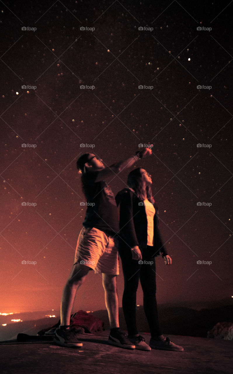 Man with a woman standing up and looking at the stars in the sky.