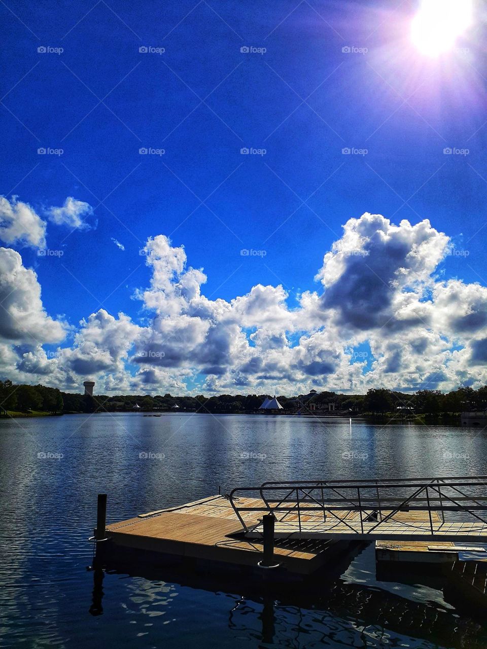 A brilliant blue sky with many clouds over the lake and dock at Cranes Roost Park in Altamonte Springs, Florida.