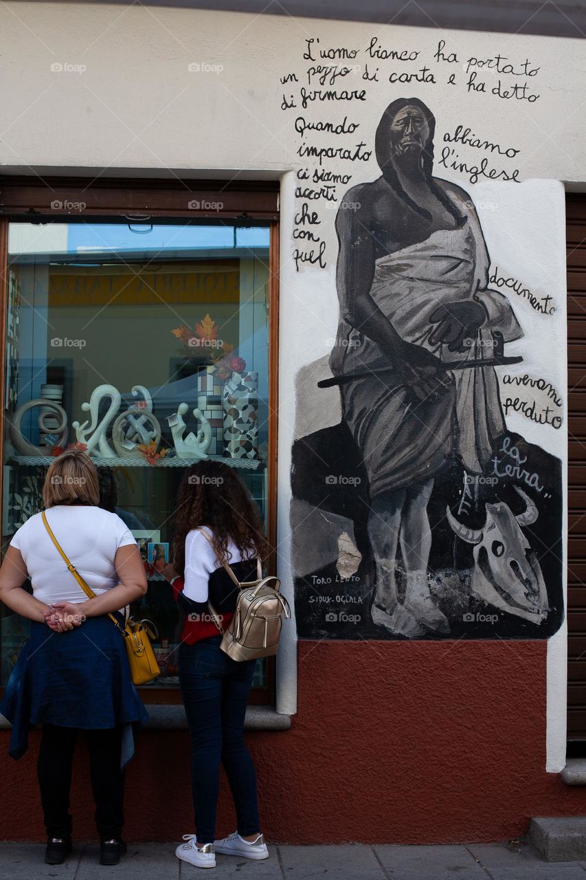 Two tourists gazing at souvenirs display case beside a mural in Orgosolo - Sardinia