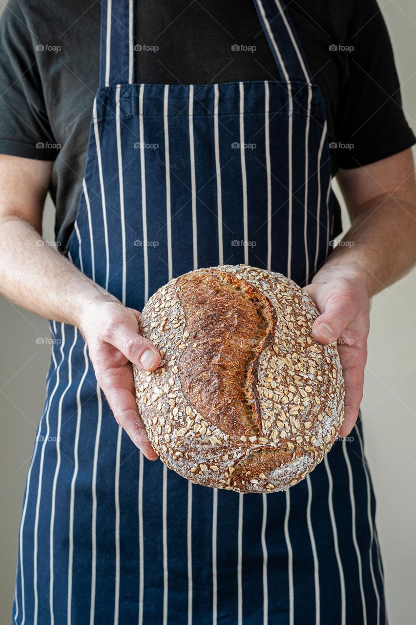 Close-up at bakers hands holding a loaf of sourdough bread in front of him.