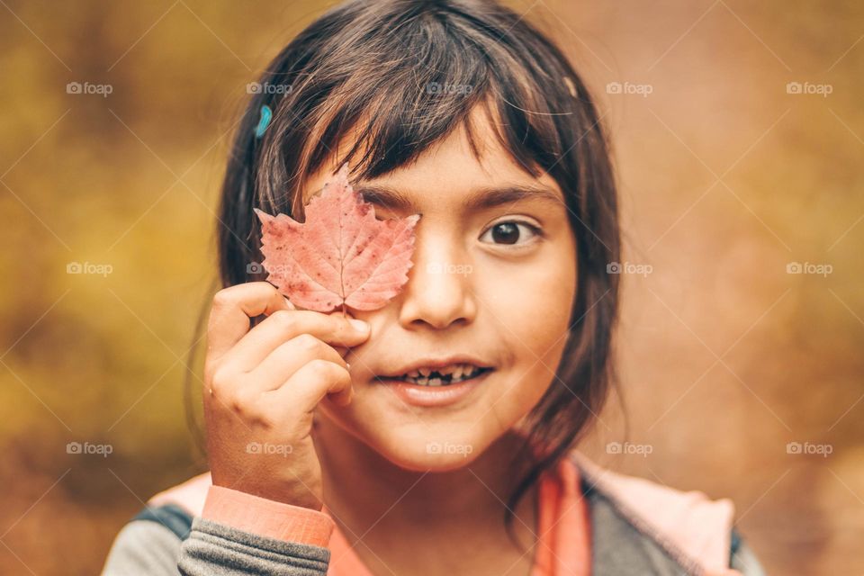Cute girl is holding an autumn leaf vlise to her eye