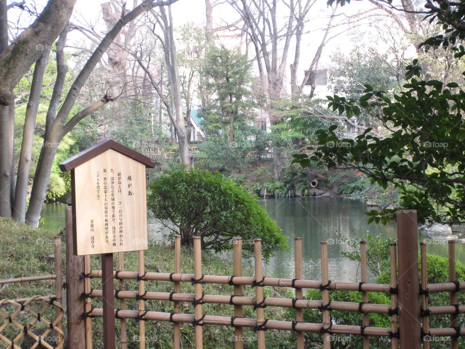 Tokyo, Japan.  Japanese Garden with Trees and Water, beside Wooden Sign with Kanji writing. Sensoji Temple. Asakusa Kannon.