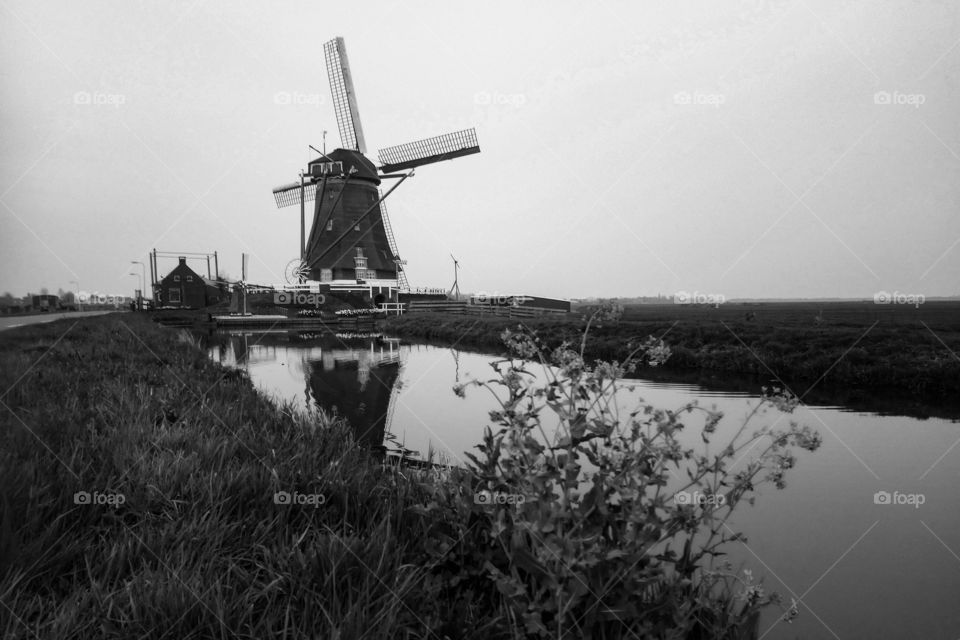 A typical dutch scene with a windmill along the water of a canal. Black and White Photograph.