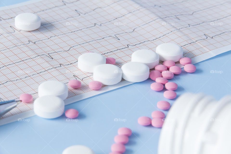 Pills and medicines lie on a blue background with an electrocardiogram of the heart.
