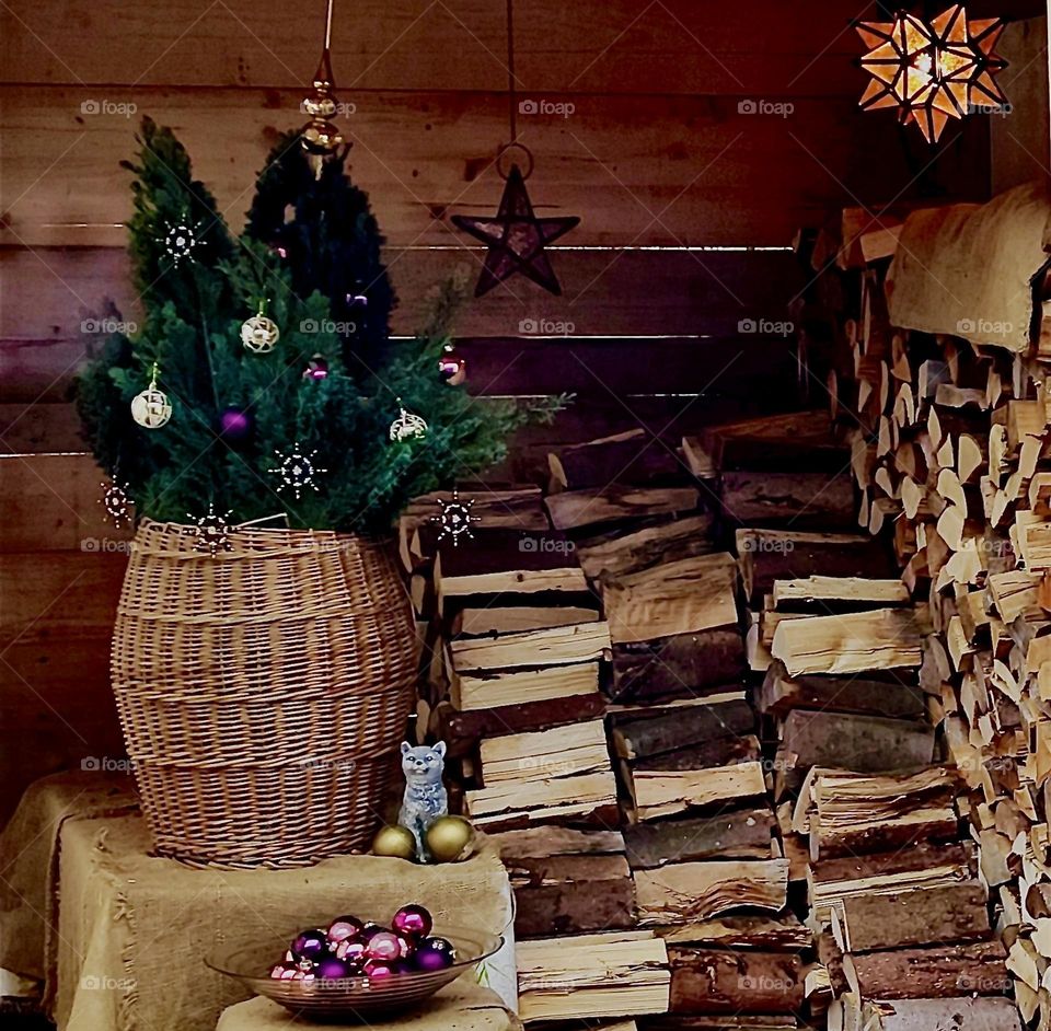 A shed in the garden of the house in “Bavaria” stores firewood in the winter stacked in four rows. A basket with evergreen twigs and shiny baubles serves as Christmas decor, a jar with more, a star, also a cat sculpture. 2023. Hypnotic Productions