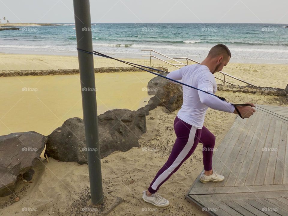 man training in the street doing various exercises with elastic band and overlooking the sea