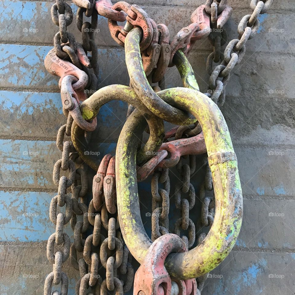 Close-up: Used powerful chains with hooks and connections hanging on metal wall with remnants of blue paint