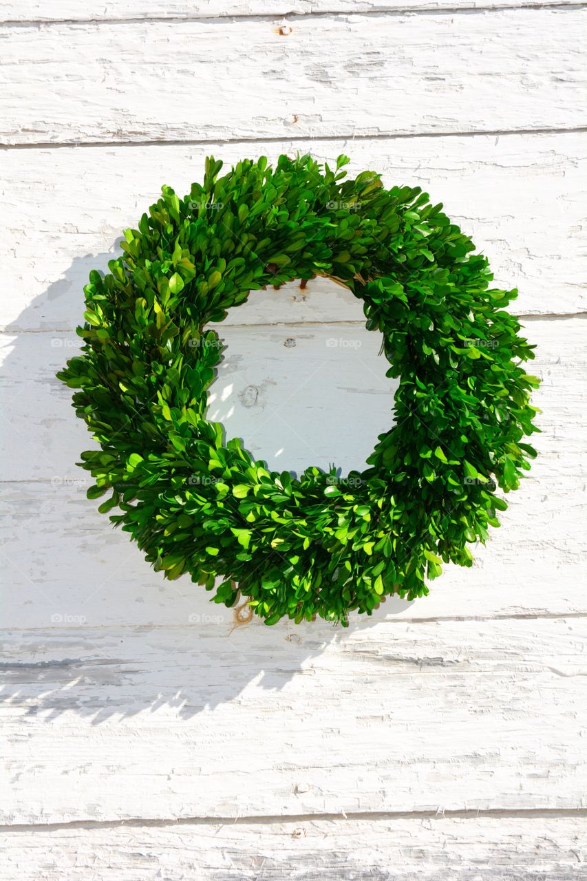 A boxwood wreath hanging on a shingled wall.