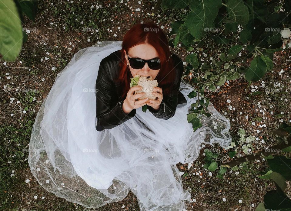 a girl enjoys a sandwich under a tree in the park