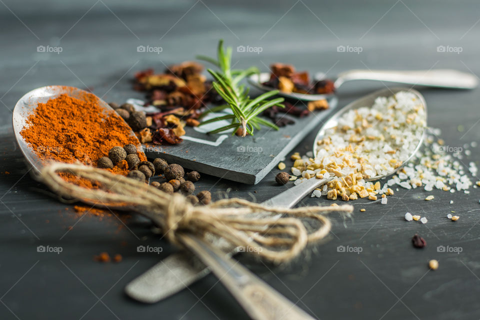herbs and spices in old, silver spoons, on a gray, stone background