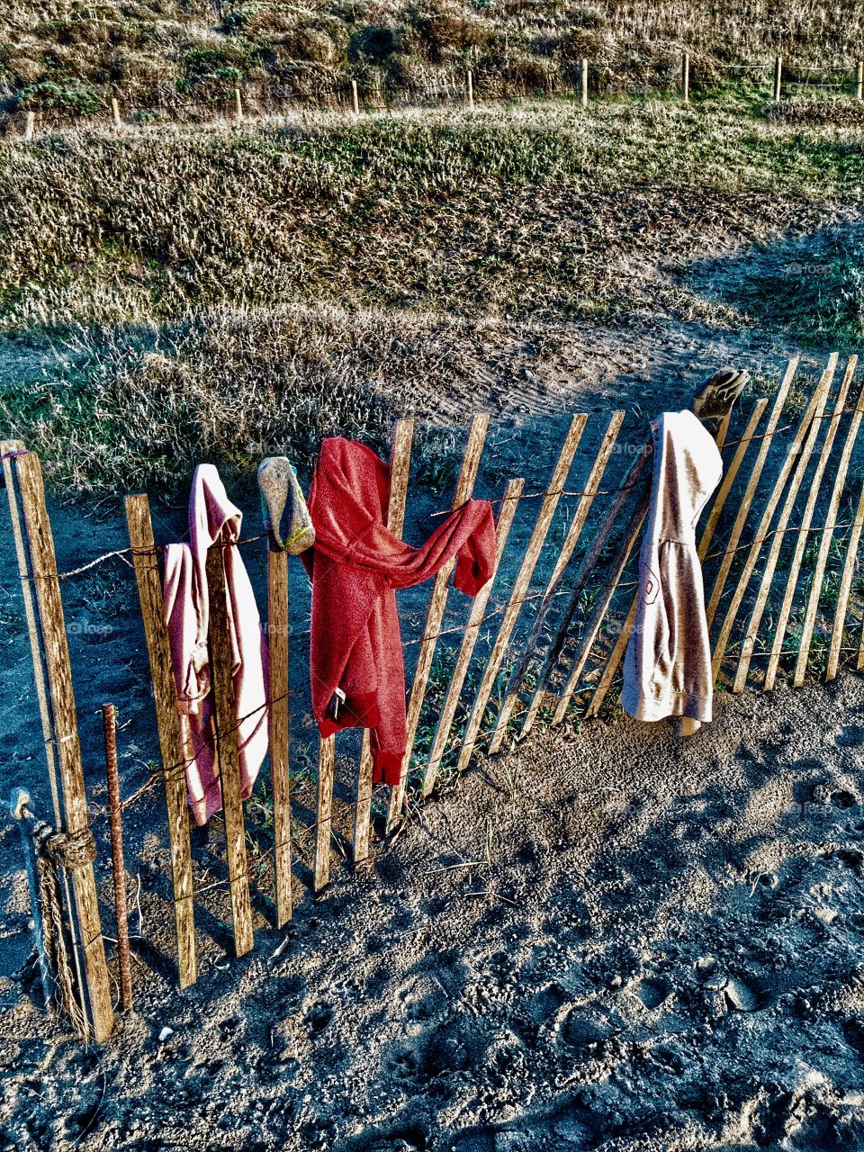 Rickety picket fence at the beach with hoodies tossed to and fro. 